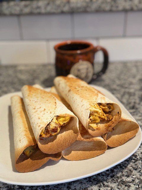 Three toasted sandwiches filled with egg and spices on a plate, with a mug in the background.