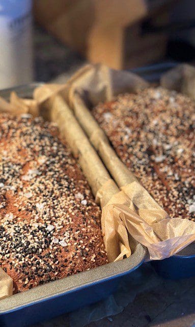 Two loaves of seeded bread in parchment-lined pans.